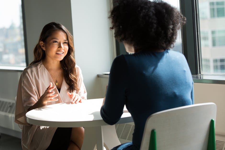 pexels-photo-1181715-1181715-1 Two women sitting at a table having a professional discussion in a bright office setting.